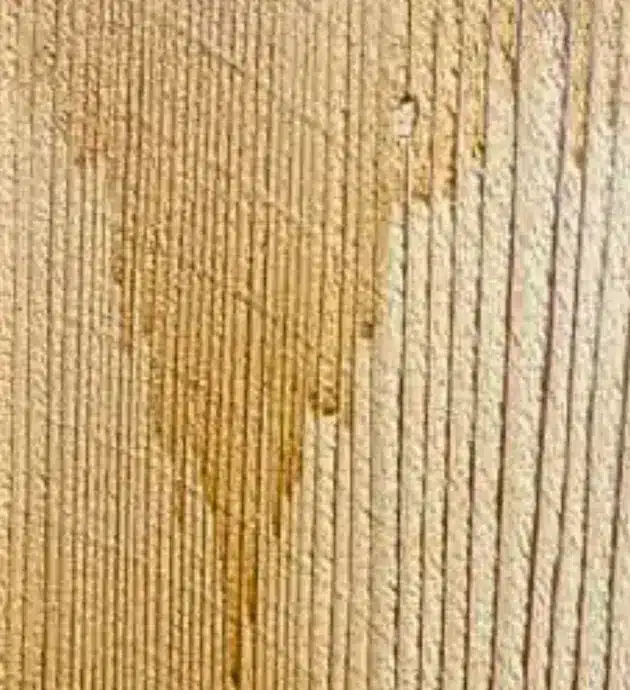 Close-up view of wood grain showing natural vertical striations and texture on a light-colored wooden surface, with subtle variations in tone and weathered areas creating depth and character typical of natural wood finishing.
